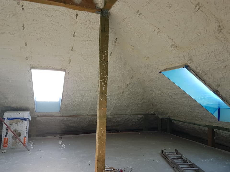 Poddasze po ociepleniu pianką PUR, widoczne okna dachowe i drewniana konstrukcja pokryta pianą. Na podłodze leżą narzędzia i materiały budowlane.