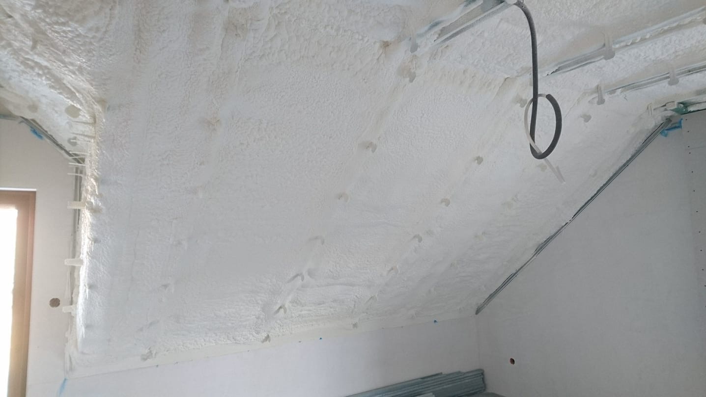 Poddasze po ociepleniu pianką PUR, widoczne równomierne pokrycie powierzchni, metalowe profile konstrukcyjne oraz fragment okna w lewym dolnym rogu.