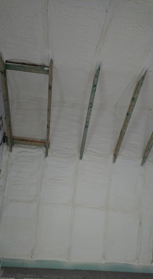 Poddasze ocieplone pianką PUR, widoczne drewniane elementy konstrukcyjne, biała, równomierna warstwa izolacji. Detal wykończenia.