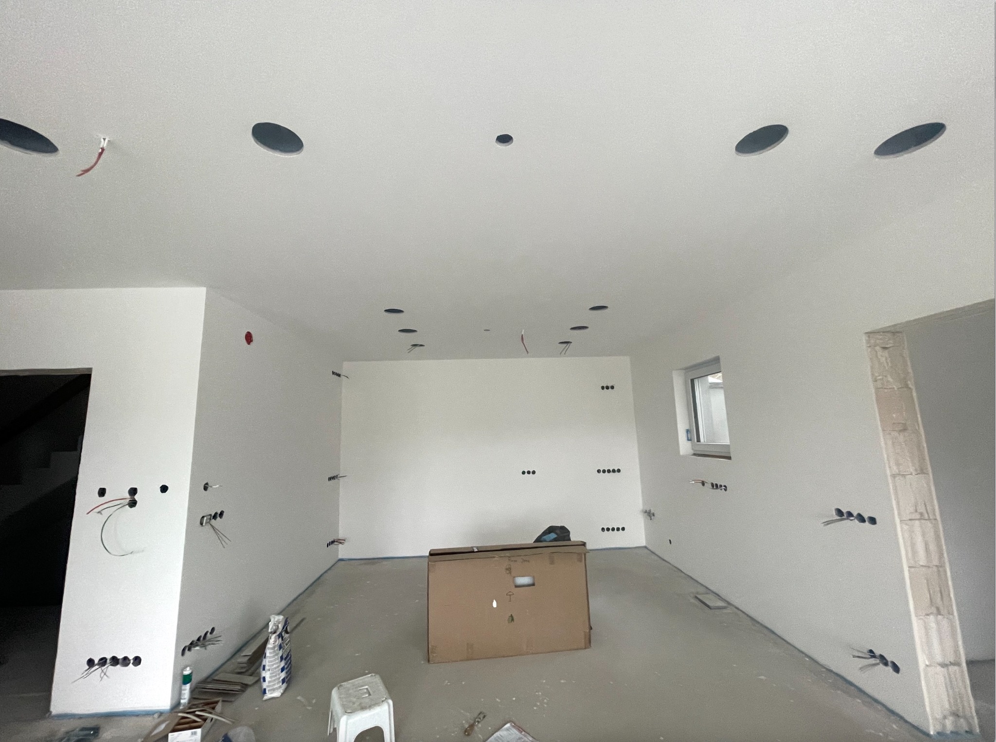 Wnętrze w trakcie prac elektrycznych: widoczne przewody, puszki instalacyjne w ścianach i suficie, przygotowane do montażu oświetlenia. Na podłodze karton i taboret.