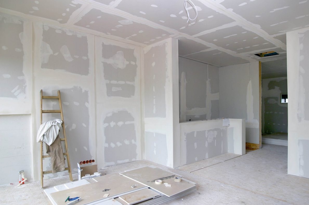 Wnętrze w trakcie prac wykończeniowych: ściany i sufit pokryte płytami gipsowo-kartonowymi, widoczne narzędzia, drabina i szpachlowane łączenia.