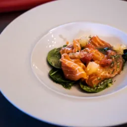 Elegancko podane carpaccio z łososia z cytrusami i szpinakiem na białym talerzu. Fine dining, zbliżenie.