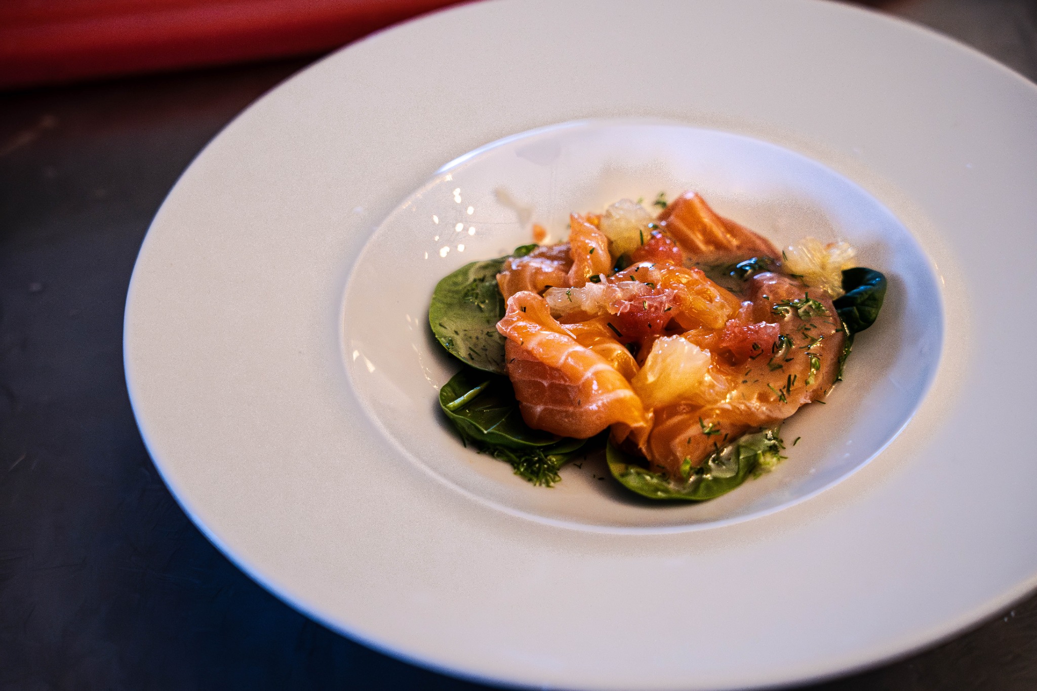 Elegancko podane carpaccio z łososia z cytrusami i szpinakiem na białym talerzu. Fine dining, zbliżenie.