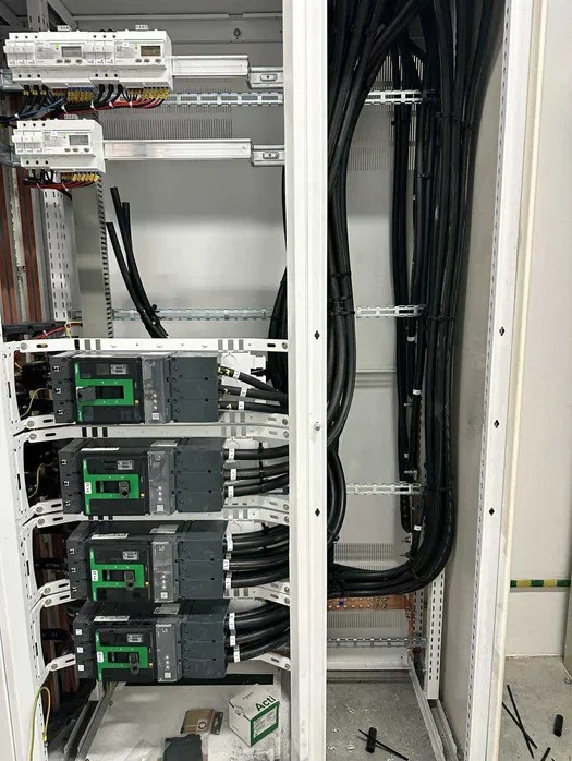 Rozdzielnica elektryczna w trakcie montażu: liczniki, bezpieczniki, przewody ułożone wewnątrz metalowej szafy. Widoczne elementy montażowe i narzędzia.