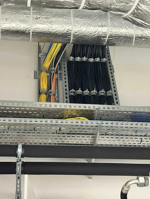 Profesjonalnie ułożone kable elektryczne w korytach i na drabinkach kablowych, z widoczną izolacją termiczną rur. Estetyczny montaż instalacji.