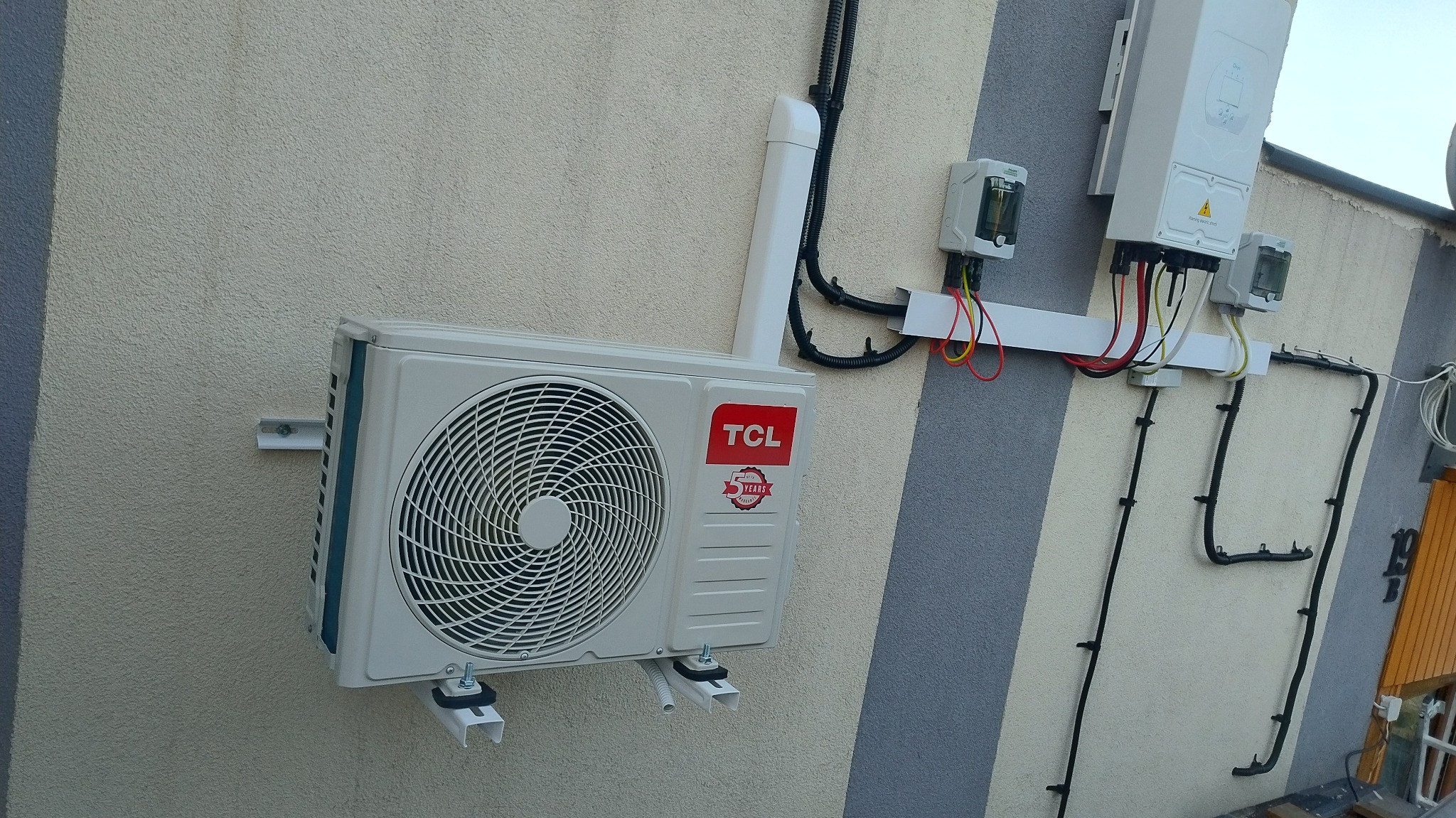 Zamontowana jednostka zewnętrzna klimatyzacji TCL z okablowaniem na elewacji budynku w Radomiu. Widoczne elementy instalacji elektrycznej i rury odprowadzające skropliny.