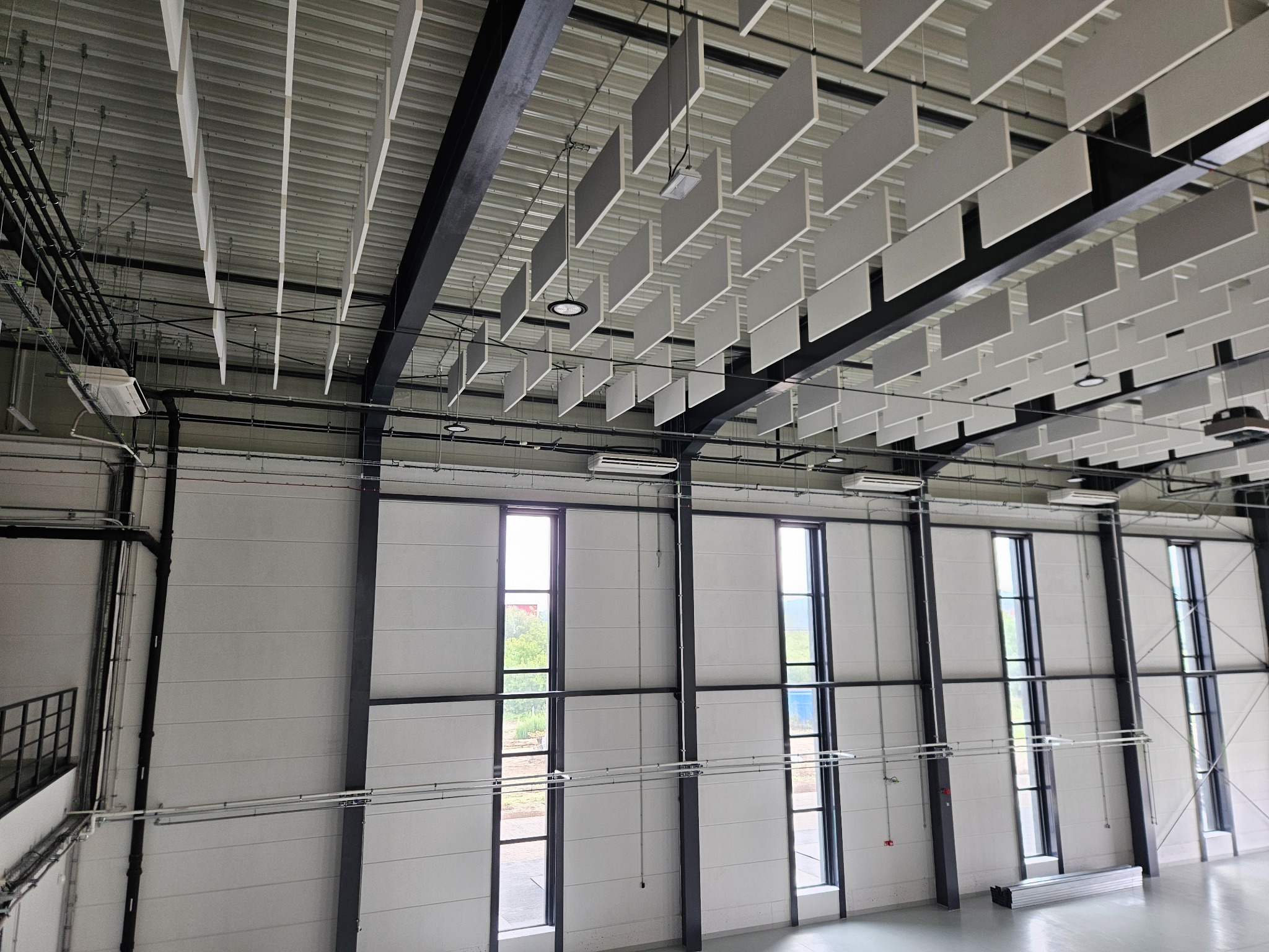 Wnętrze hali biurowej z zamontowanymi panelami sufitowymi i klimatyzacją. Widoczne okna, instalacje i metalowa konstrukcja. Oświetlenie sufitowe.