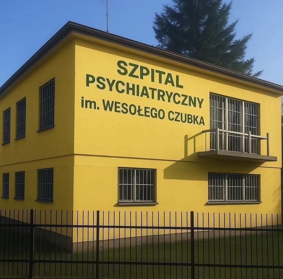 Żółty budynek szpitala psychiatrycznego z napisem 'Szpital Psychiatryczny im. Wesołego Czubka', okna z kratami i czarne metalowe ogrodzenie.