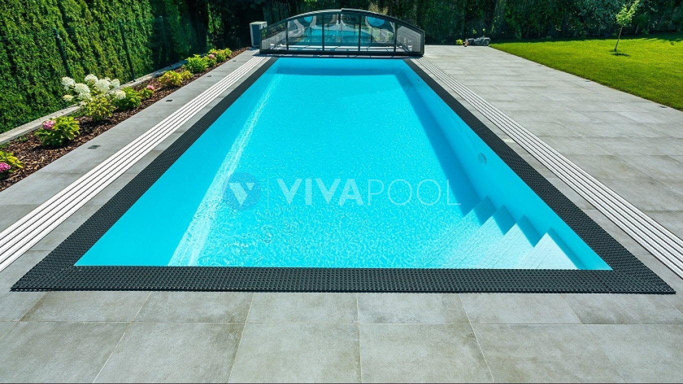 Prostokątny basen z turkusową wodą, obłożony szarymi płytami i czarną mozaiką, z częściowo zasłoniętym zadaszeniem w tle ogrodu.