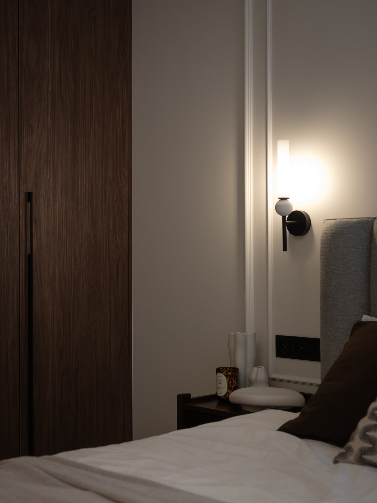 Nowoczesna sypialnia w Krakowie: drewniana szafa z długim uchwytem, minimalistyczna lampka nocna i dekoracje na szafce. Subtelne oświetlenie.