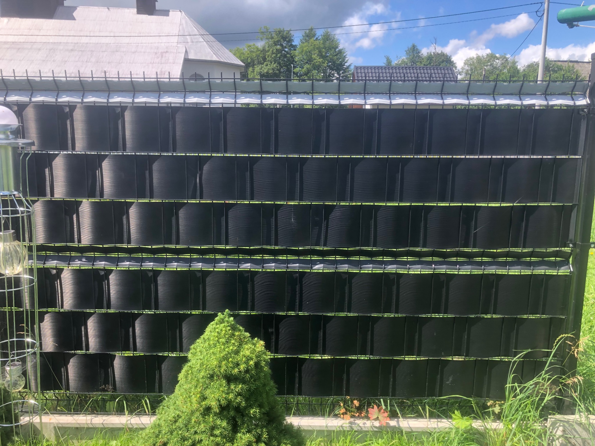 Nowoczesne ogrodzenie panelowe z czarnym wypełnieniem, widoczne zza zieleni. Montaż ogrodzeń w Nowym Targu.