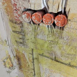 Brespol - Ściana z siatką wzmacniającą, widoczne pomarańczowe rury instalacji elektrycznej i przewody. Fragment ściany przygotowany do dalszych prac wykończeniowych.