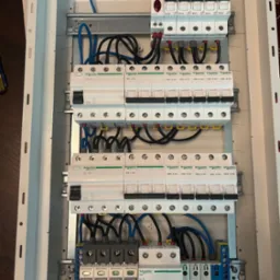 Rozdzielnica elektryczna z zamontowanymi bezpiecznikami i przewodami, widok z góry, różne marki Schneider i Schellinger. Elementy zabezpieczające w skrzynce.