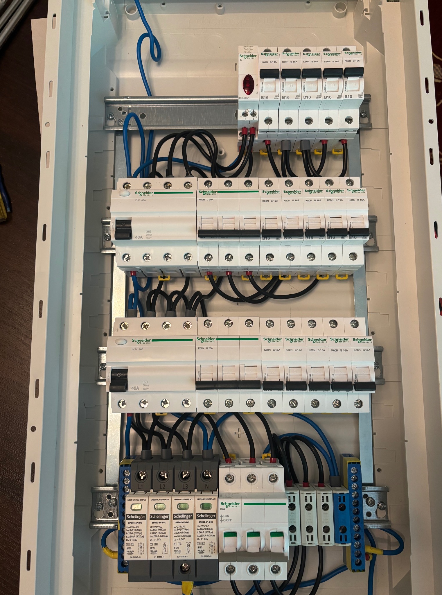 Rozdzielnica elektryczna z zamontowanymi bezpiecznikami i przewodami, widok z góry, różne marki Schneider i Schellinger. Elementy zabezpieczające w skrzynce.