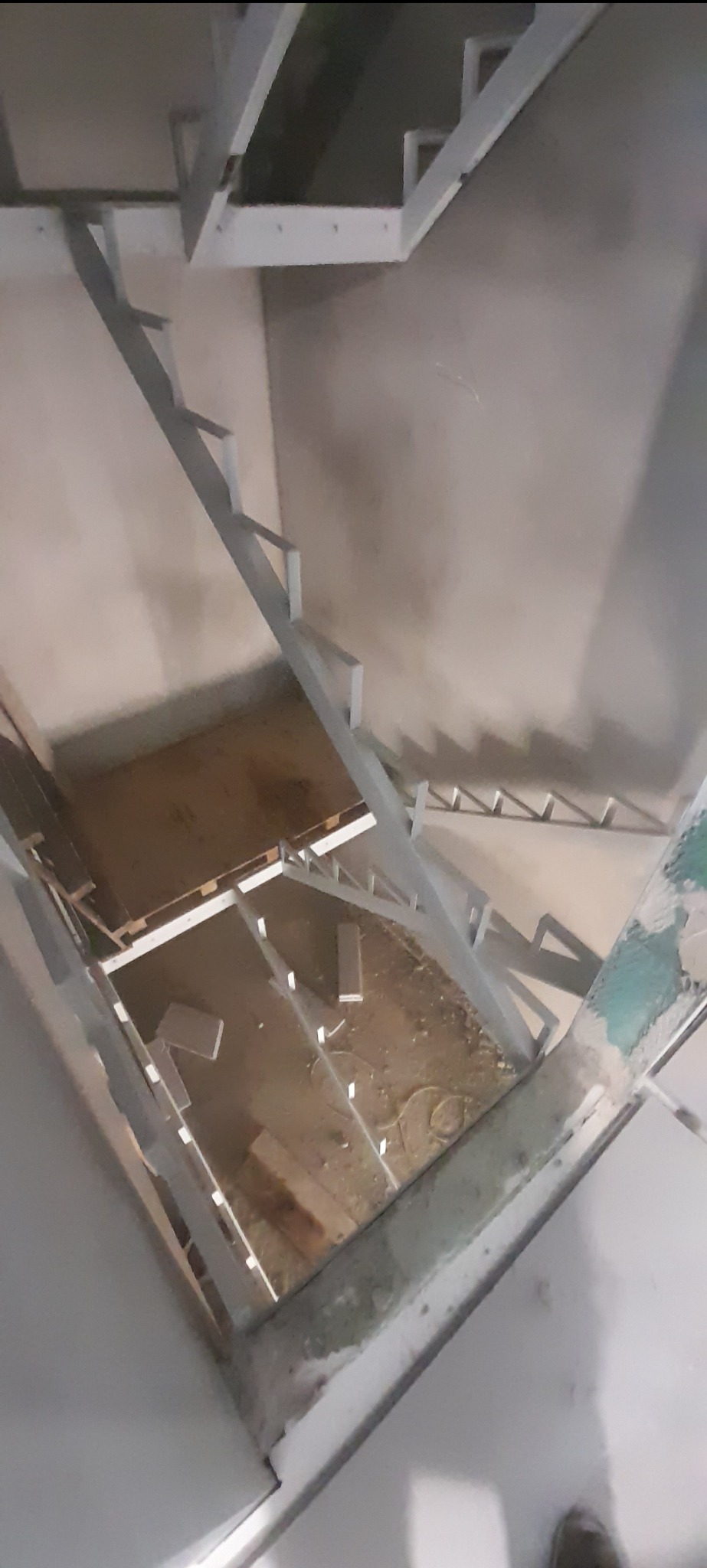 Wysoki kąt: konstrukcja schodów metalowych z profilami, widoczne elementy mocujące i surowy stan wnętrza. W tle ściana i podłoga w trakcie budowy.