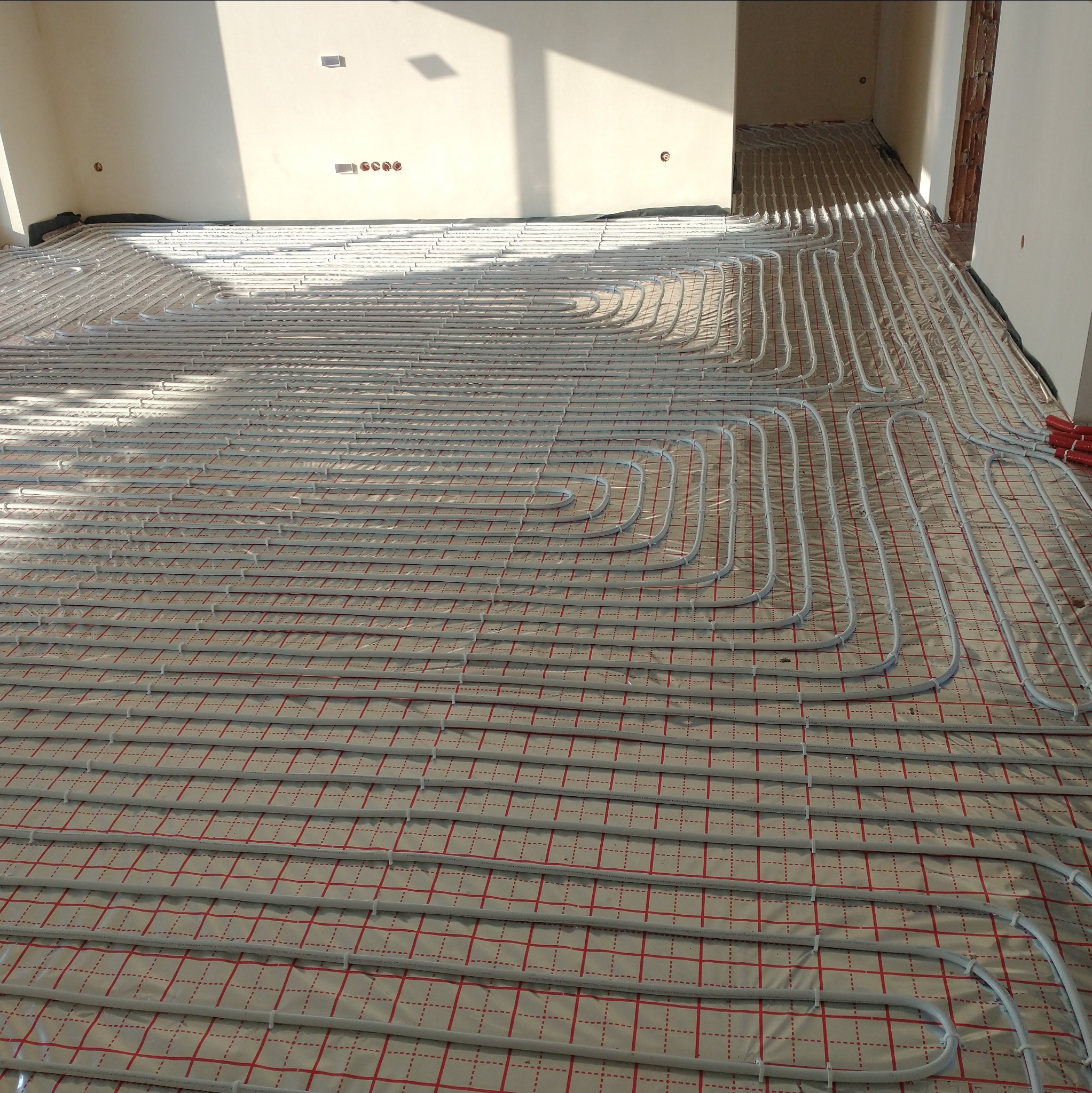 Ułożone rury ogrzewania podłogowego na folii z siatką w nowym budynku, widok z góry, jasne światło dzienne.
