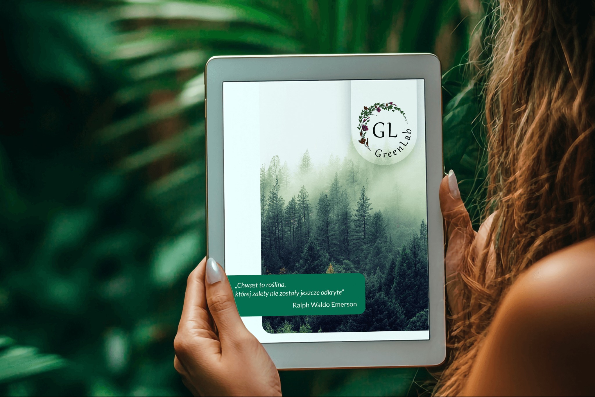 Kobieta trzyma tablet z logo GreenLab i cytatem Emersona na tle mglistego lasu. Tablet w dłoniach na tle zieleni, z widocznymi włosami modelki.