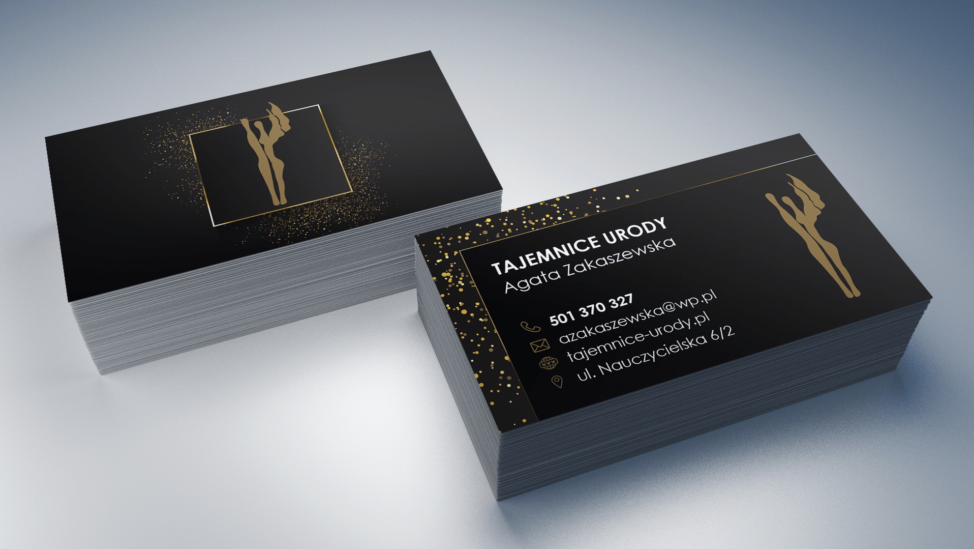 Stosy czarno-złotych wizytówek z logo figury kobiety w kwadracie, prezentujące dane kontaktowe 'Tajemnice Urody' Agaty Zakaszewskiej, na gładkim tle.