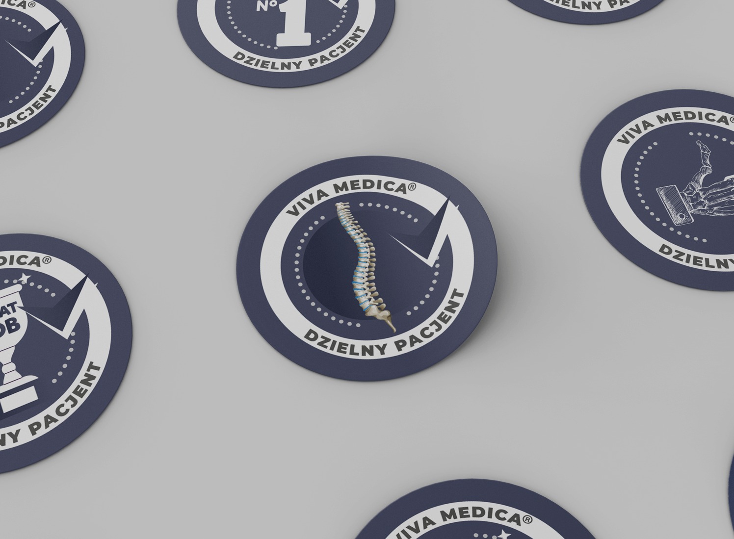 Kolekcja okrągłych naklejek Viva Medica z różnymi grafikami: kręgosłup, puchar, dłoń-szkielet, numer 1. Napis: Dzielny Pacjent, na szarym tle.
