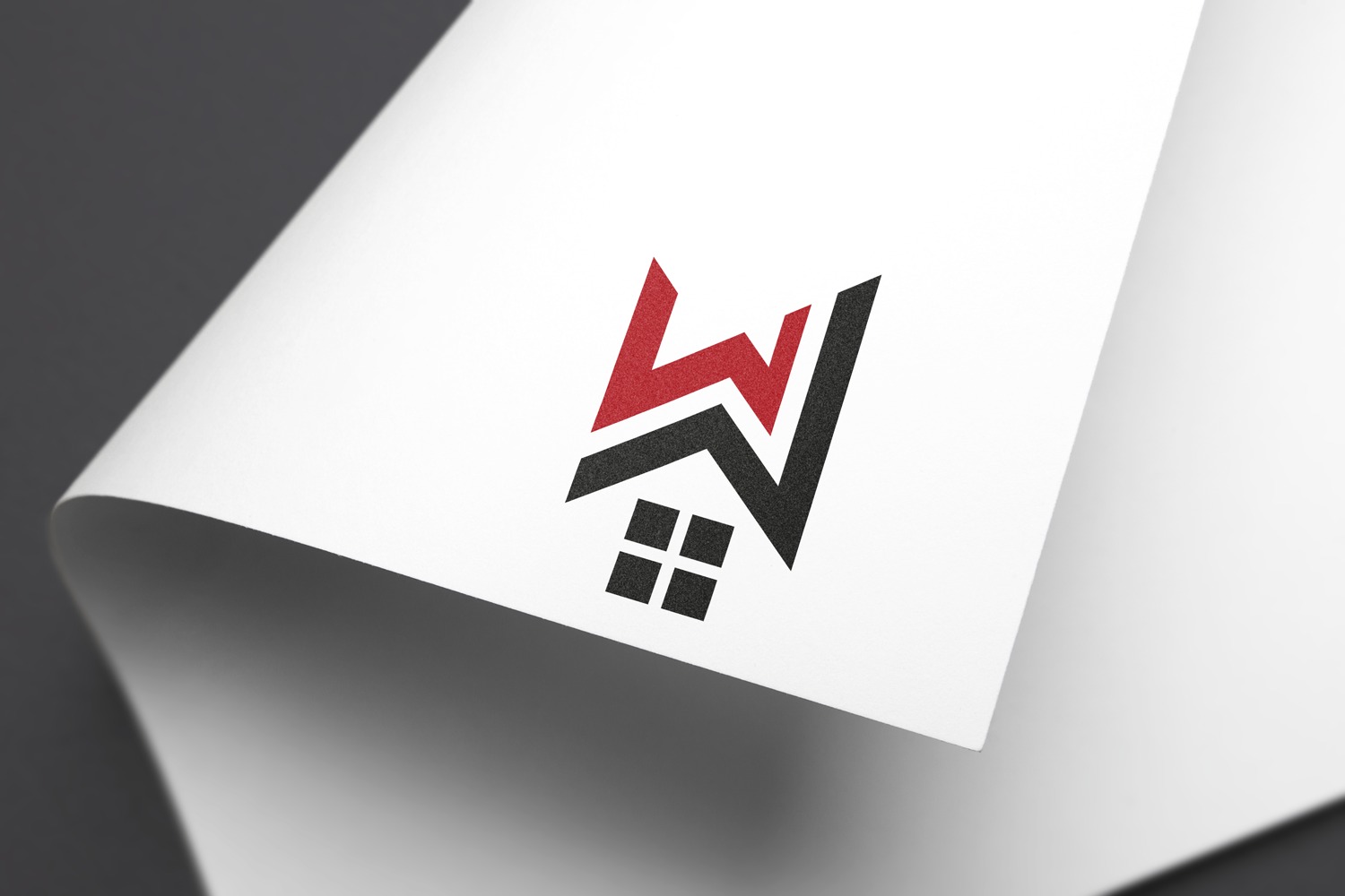 Logo z motywem domu w kolorach czerwonym i czarnym, umieszczone na białej kartce z delikatnym cieniem, ukazane z bliska pod kątem.