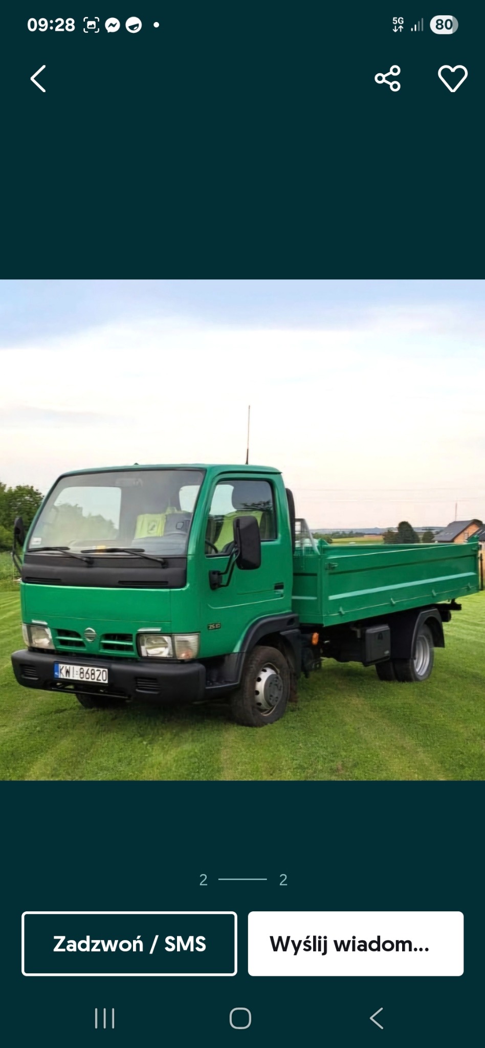 Zielona wywrotka Nissan Cabstar 2.5TD na trawiastym terenie. Widoczna tablica rejestracyjna KWI 86820. Samochód stoi na tle zieleni i jasnego nieba.