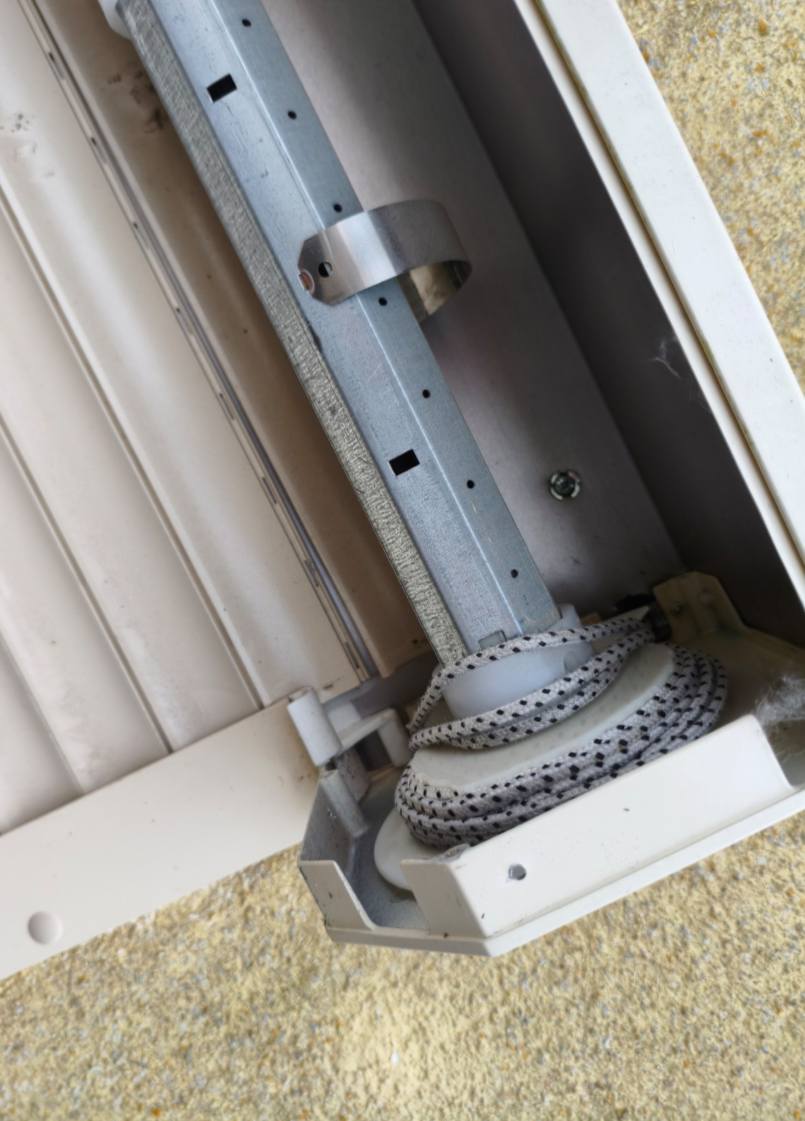 Mechanizm zwiniętej linki rolety w beżowej obudowie, widok z góry, ukazujący detale konstrukcyjne i zużycie materiału.