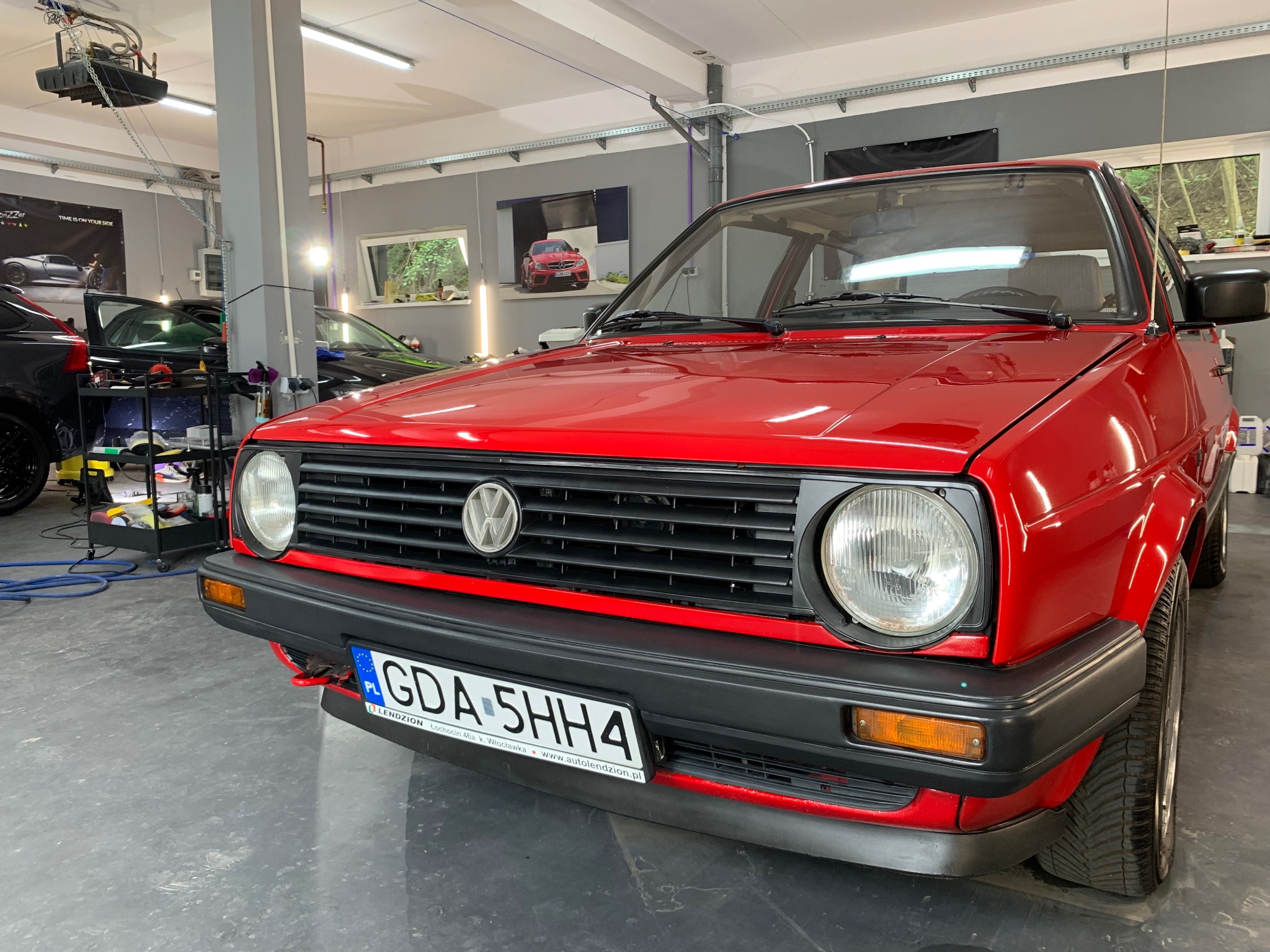 Czerwony Volkswagen Golf II po detailingu, błyszczący lakier, widoczna tablica rejestracyjna GDA 5HH4, wnętrze myjni z oknem i plakatem motoryzacyjnym w tle.