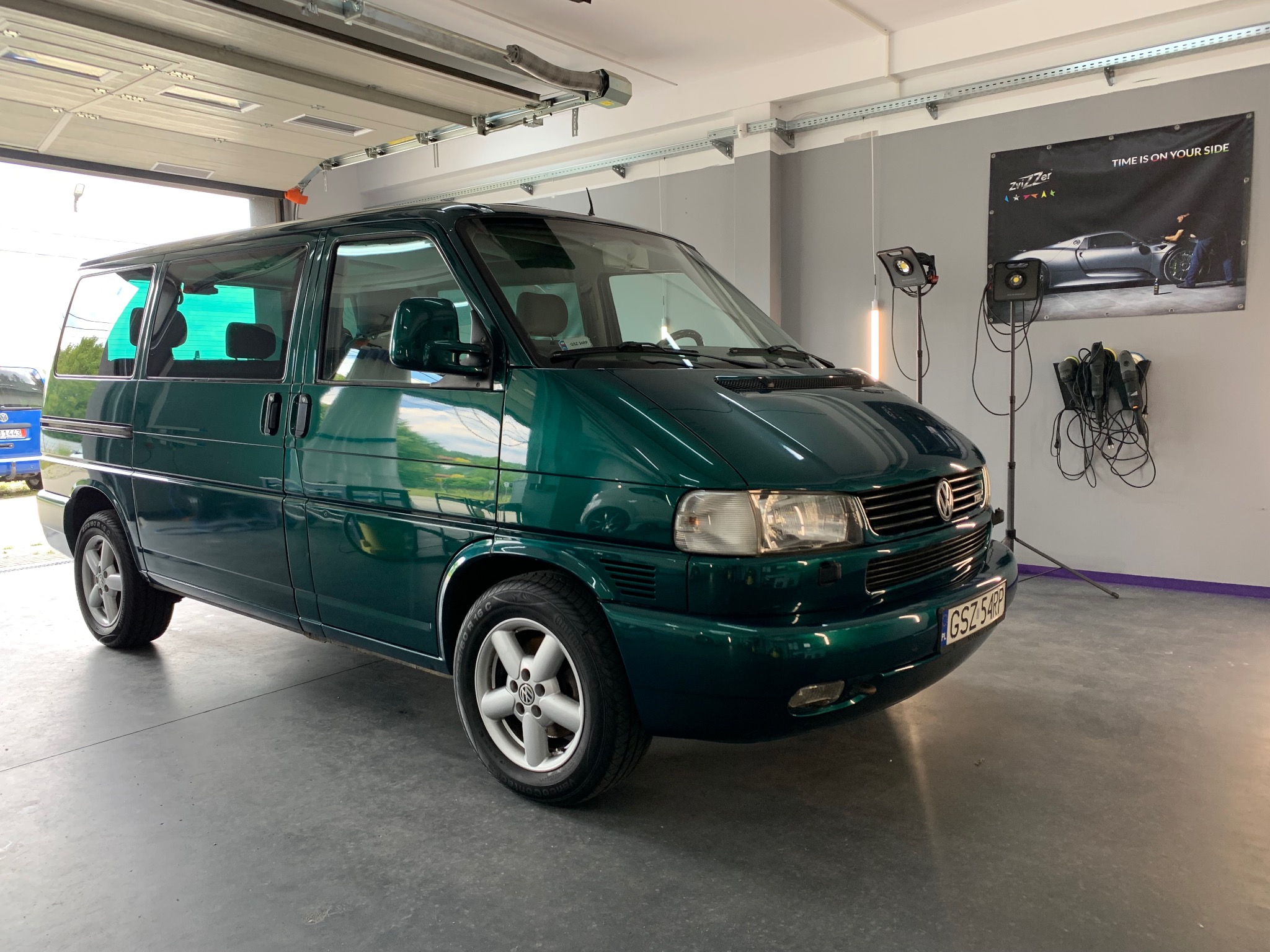 Zielony bus VW T4 po detailingu w myjni, widoczne polerki i lampy. Plakat z hasłem 'Time is on your side'. Błyszczące lakierowanie.