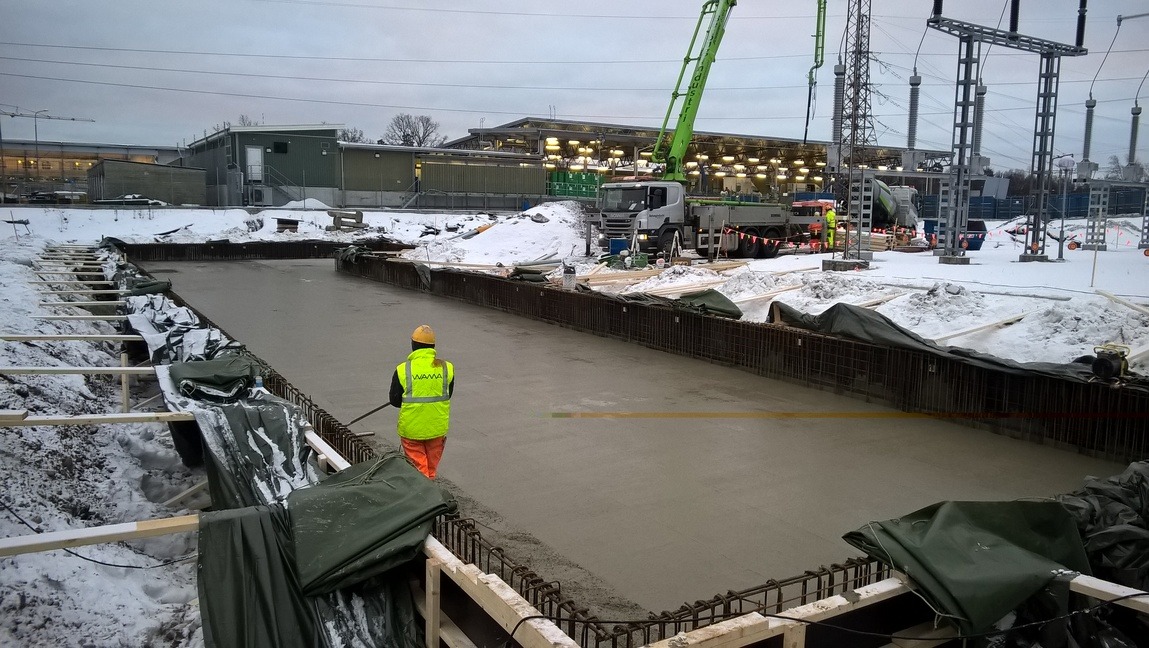 Wylewanie betonu na przygotowany fundament w zimowych warunkach. Widoczny pracownik w odblaskowej kamizelce i pompa do betonu w tle.