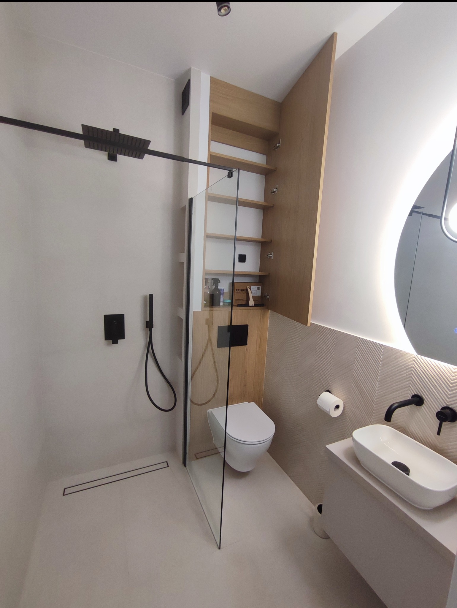 Nowoczesna łazienka z kabiną typu walk-in, wiszącą toaletą i umywalką nablatową. Uwagę zwraca drewniana szafka w zabudowie i oświetlenie lustra.