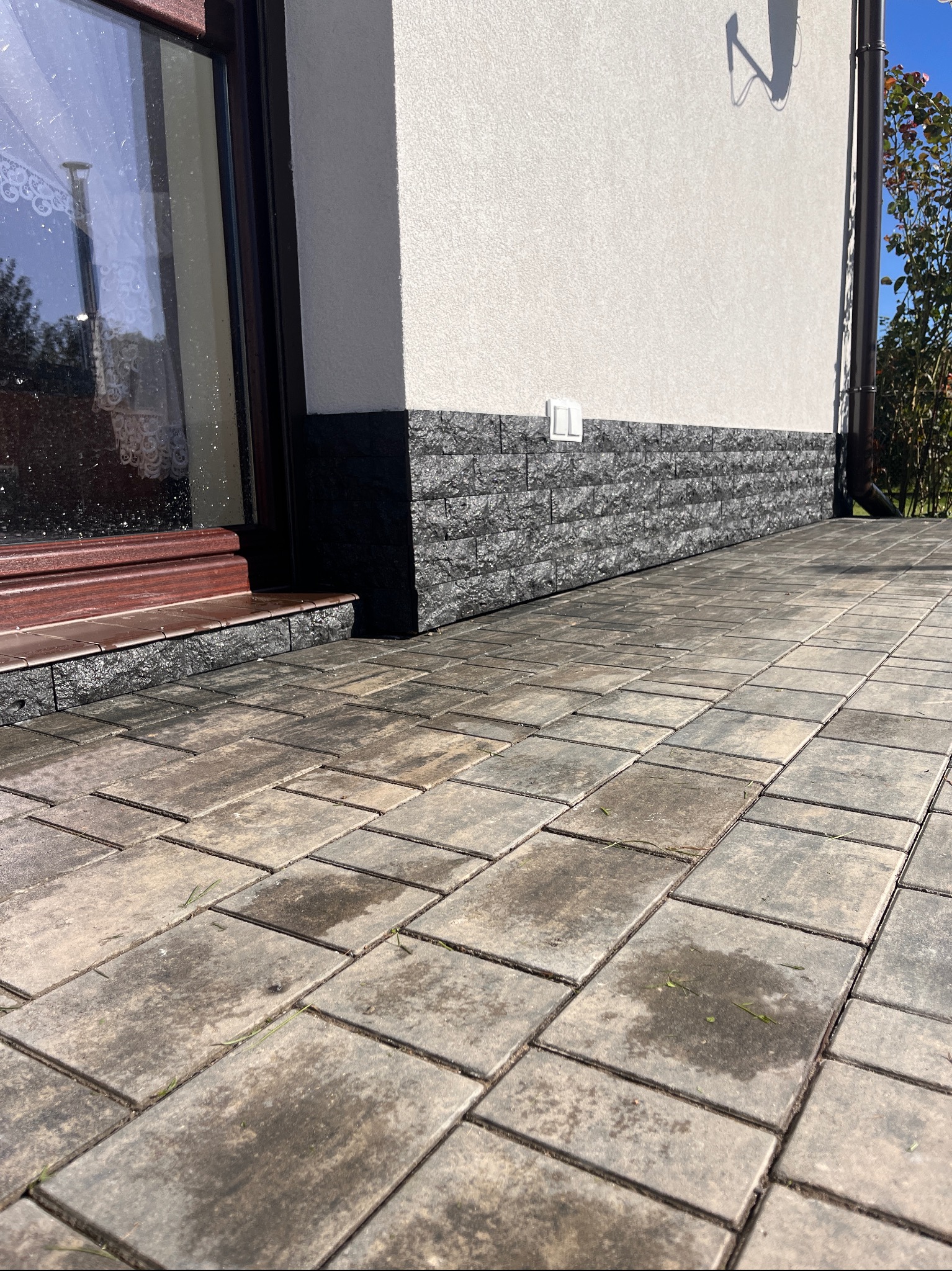 Ułożona kostka brukowa w Żywcu, z ciemną podmurówką i fragmentem elewacji budynku w tle. Widoczne detale kostki i fugi, oświetlenie dzienne.