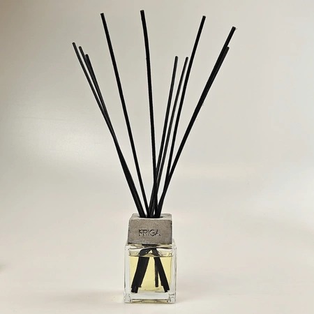 Aromatyzer z czarnymi patyczkami w szklanym flakonie z szarą, betonową podstawą z napisem FRIGA na jasnym tle. Elegancki dodatek do wnętrz.