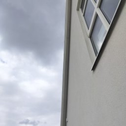 Fast Bygg - Szary budynek z białymi ramami okiennymi i szarym niebem w tle, widziany z dołu pod kątem, prezentuje minimalistyczny design i nowoczesne wykończenie elewacji.