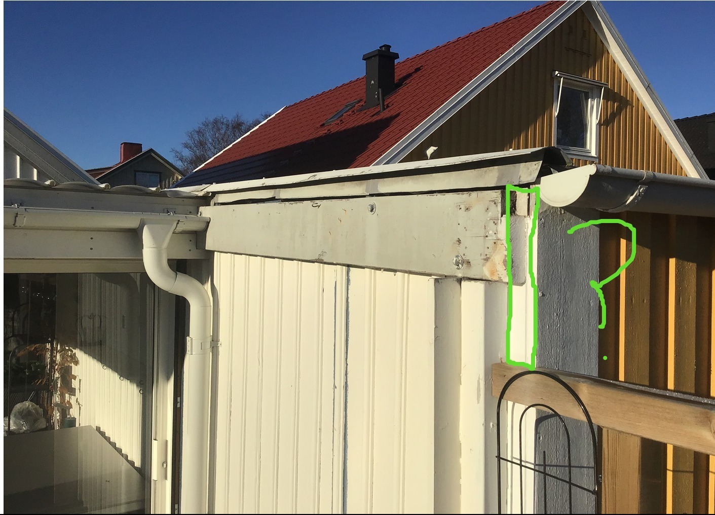 Fragment elewacji budynku z widocznymi elementami drewnianymi i orynnowaniem. Widoczny fragment dachu z czerwonymi dachówkami i kominem. Słoneczny dzień.