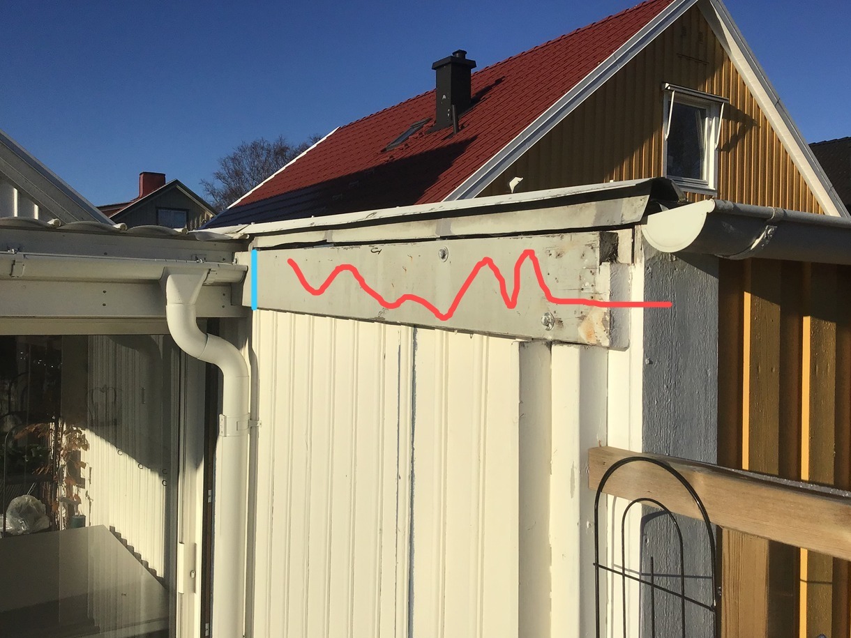 Fragment elewacji z widocznymi elementami konstrukcyjnymi dachu i rynną, w jasnym świetle słonecznym. Widoczne uszkodzenia i ślady po naprawach.