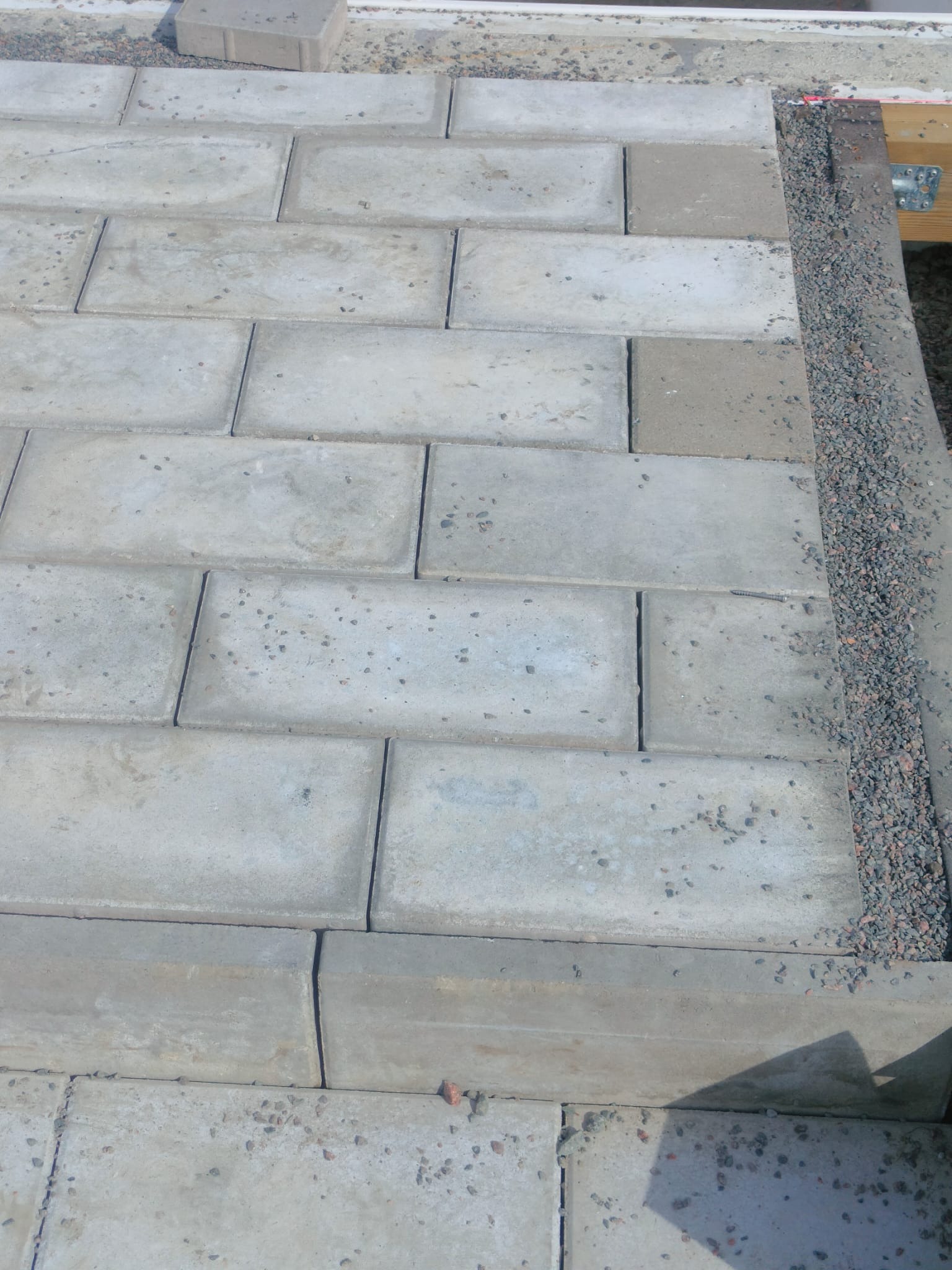 Ułożona kostka brukowa w szarym odcieniu, obrzeże z grysu, widoczne elementy konstrukcji drewnianej. Budowa tarasu.