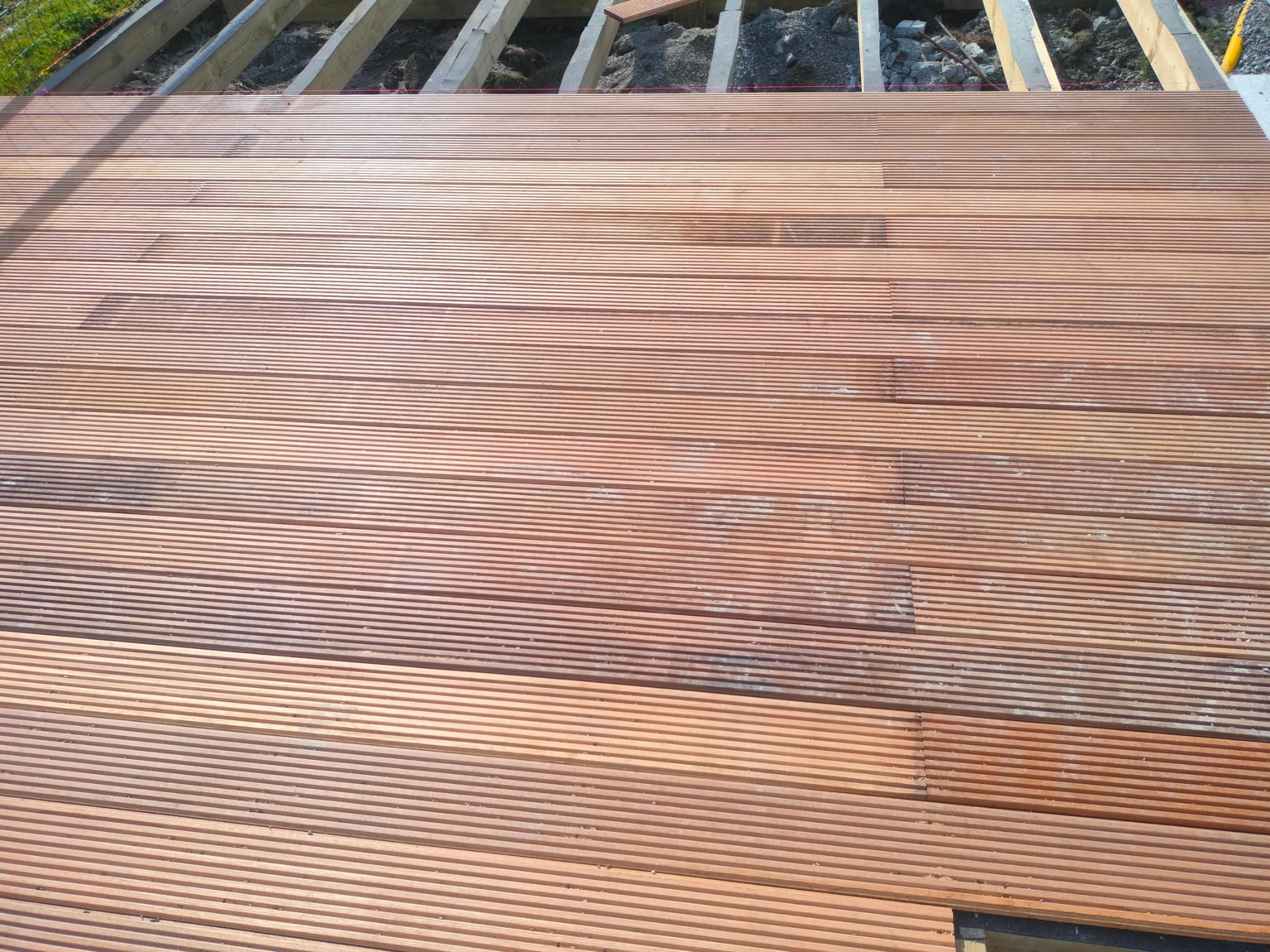 Układanie desek ryflowanych na drewnianej konstrukcji tarasu. Widoczne elementy podkonstrukcji i częściowo ułożona powierzchnia z drewna.