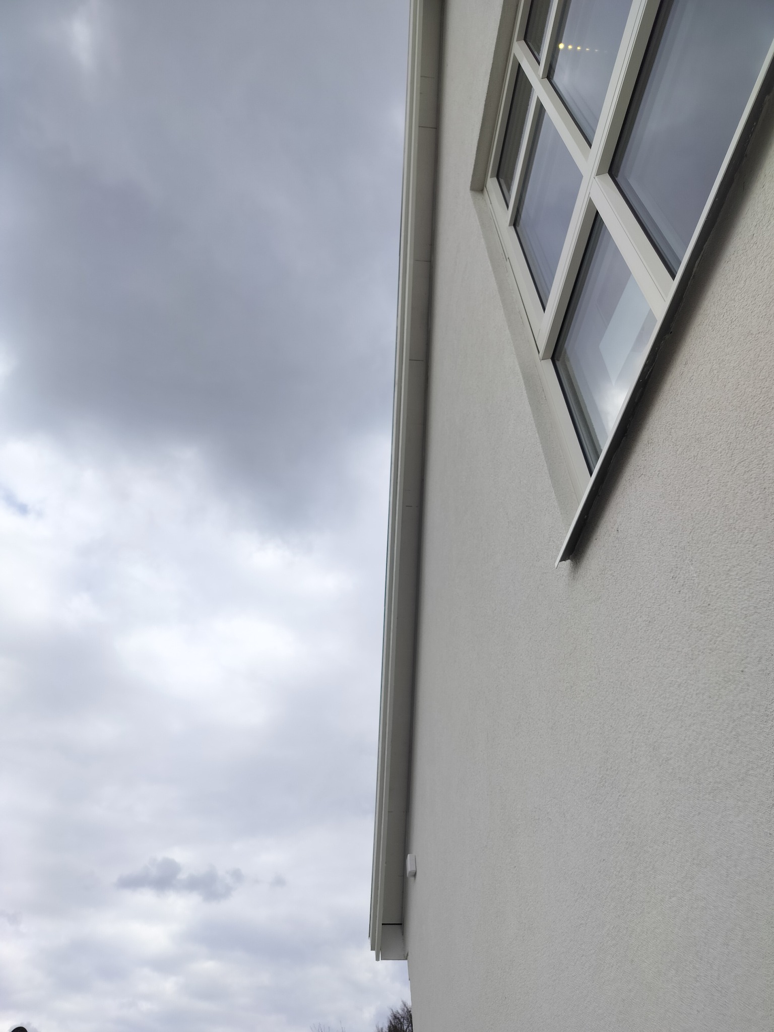Szary budynek z białymi ramami okiennymi i szarym niebem w tle, widziany z dołu pod kątem, prezentuje minimalistyczny design i nowoczesne wykończenie elewacji.