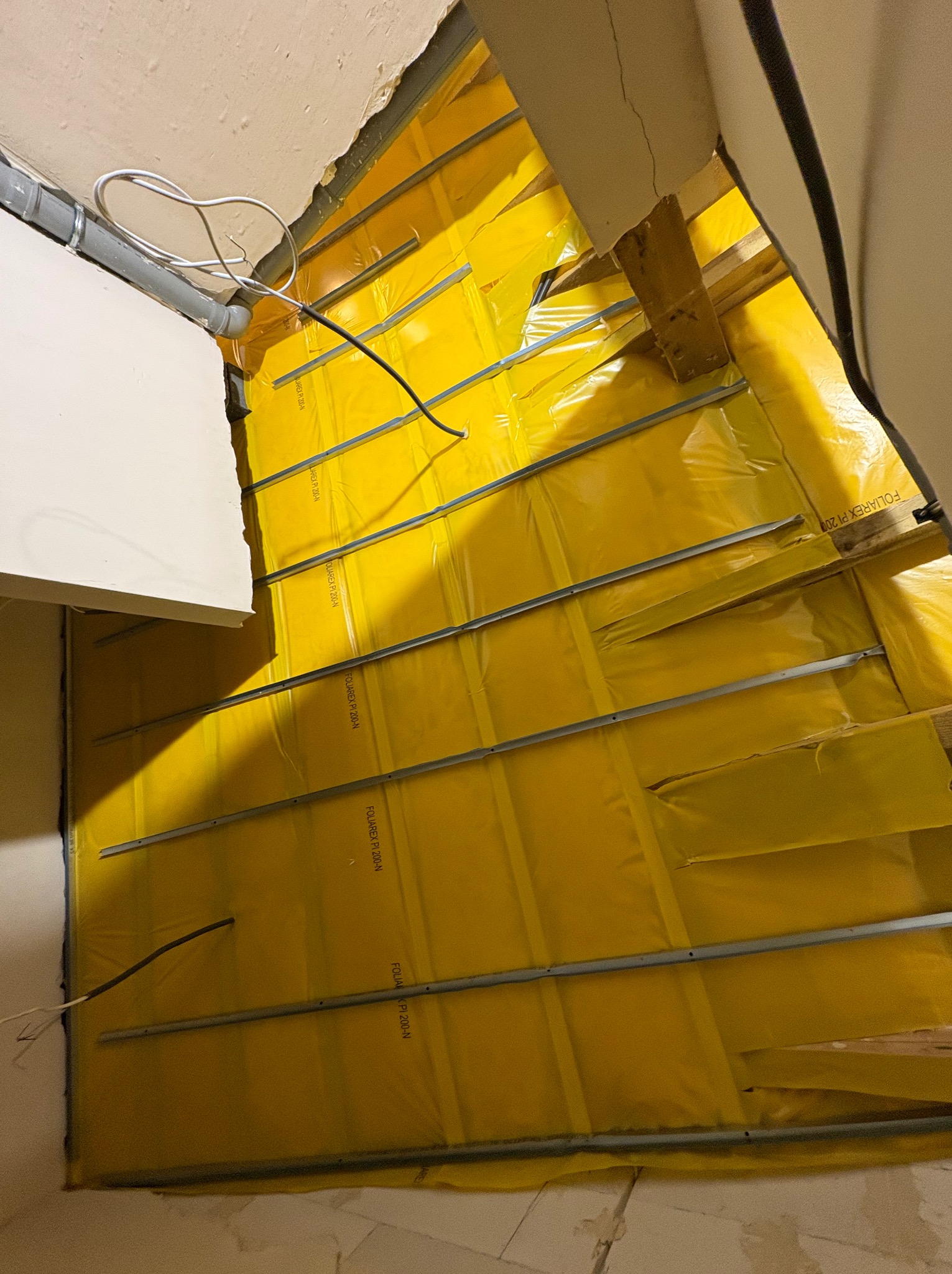 Żółta folia paroizolacyjna FOLAREX PI 200-N, zamontowana na metalowych profilach w ocieplanym poddaszu. Widoczne fragmenty instalacji elektrycznej i rury wentylacyjnej.