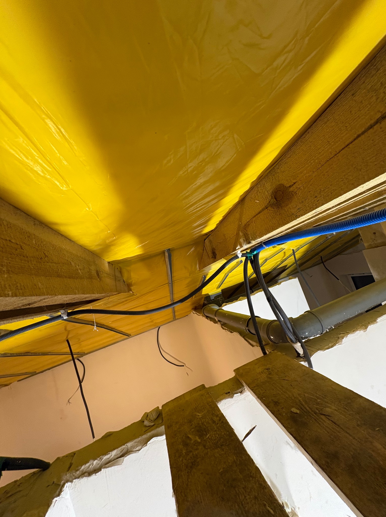 Żółta folia paroizolacyjna na poddaszu w Imielinie, widoczne drewniane belki i instalacje elektryczne. Ujęcie z dołu, ukazujące detale izolacji i prowadzenia przewodów.