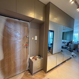 Przemysław Kotowicz - Montaż szafy wnękowej z lustrami w przedpokoju. Drzwi wejściowe zabezpieczone folią malarską. Widoczne ślady prac wykończeniowych na podłodze.