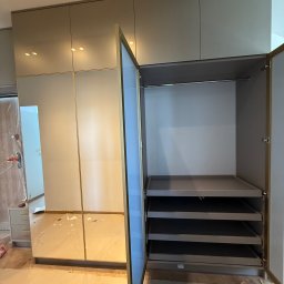 Przemysław Kotowicz - Beżowa szafa wnękowa z lustrzanymi drzwiami i złotymi detalami. Wnętrze szafy z półkami i drążkiem na ubrania. Widoczne ślady montażu.