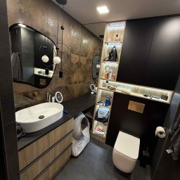 Przemysław Kotowicz - Nowoczesna łazienka z umywalką nablatową, szafką z drewnianymi frontami i czarnymi akcentami. Lustro z oświetleniem i półki z podświetleniem LED.