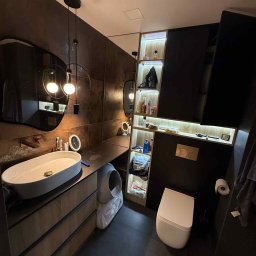 Przemysław Kotowicz - Nowoczesna łazienka z umywalką nablatową, szafką z drewnianymi frontami i oświetleniem punktowym. Ciemne płytki i minimalistyczny design tworzą elegancką przestrzeń.