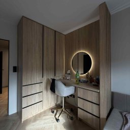 Przemysław Kotowicz - Jasna, drewniana szafa z czarnymi uchwytami i toaletka z okrągłym lustrem LED. Krzesło na złotych kółkach, parkiet w jodełkę. Nowoczesny design.