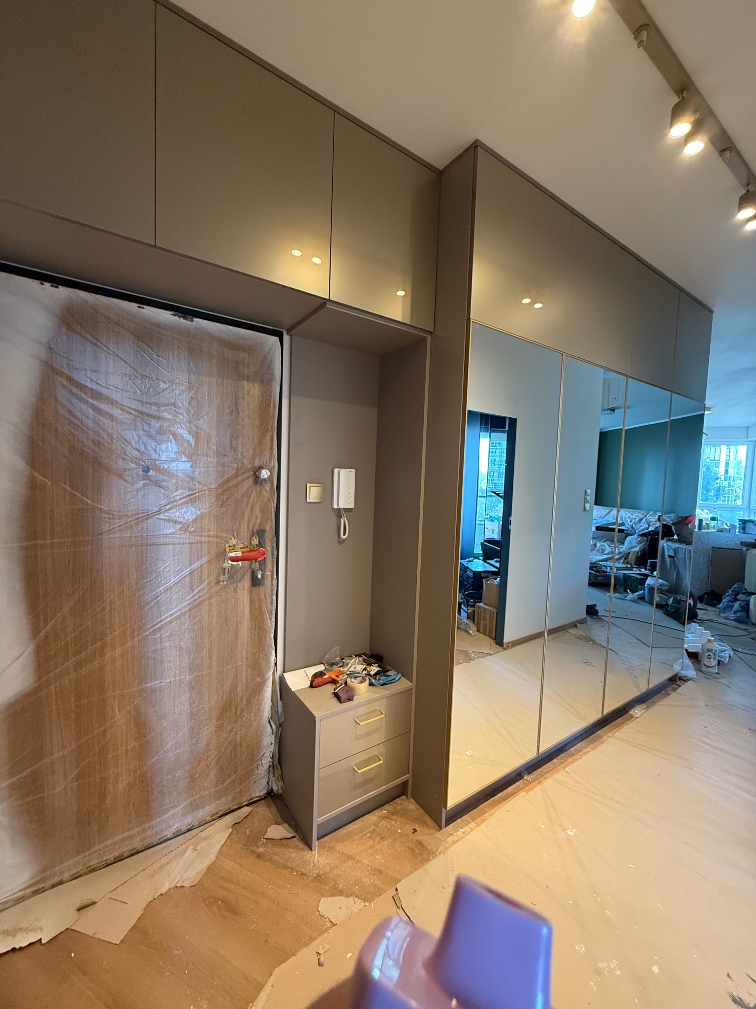 Montaż szafy wnękowej z lustrami w przedpokoju. Drzwi wejściowe zabezpieczone folią malarską. Widoczne ślady prac wykończeniowych na podłodze.