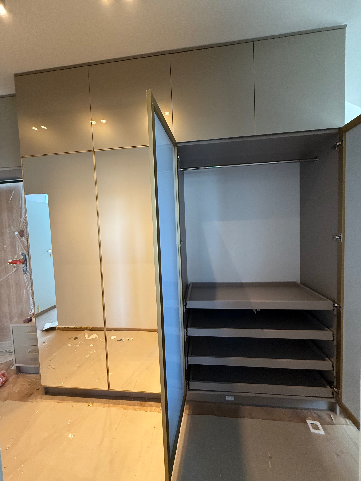 Beżowa szafa wnękowa z lustrzanymi drzwiami i złotymi detalami. Wnętrze szafy z półkami i drążkiem na ubrania. Widoczne ślady montażu.