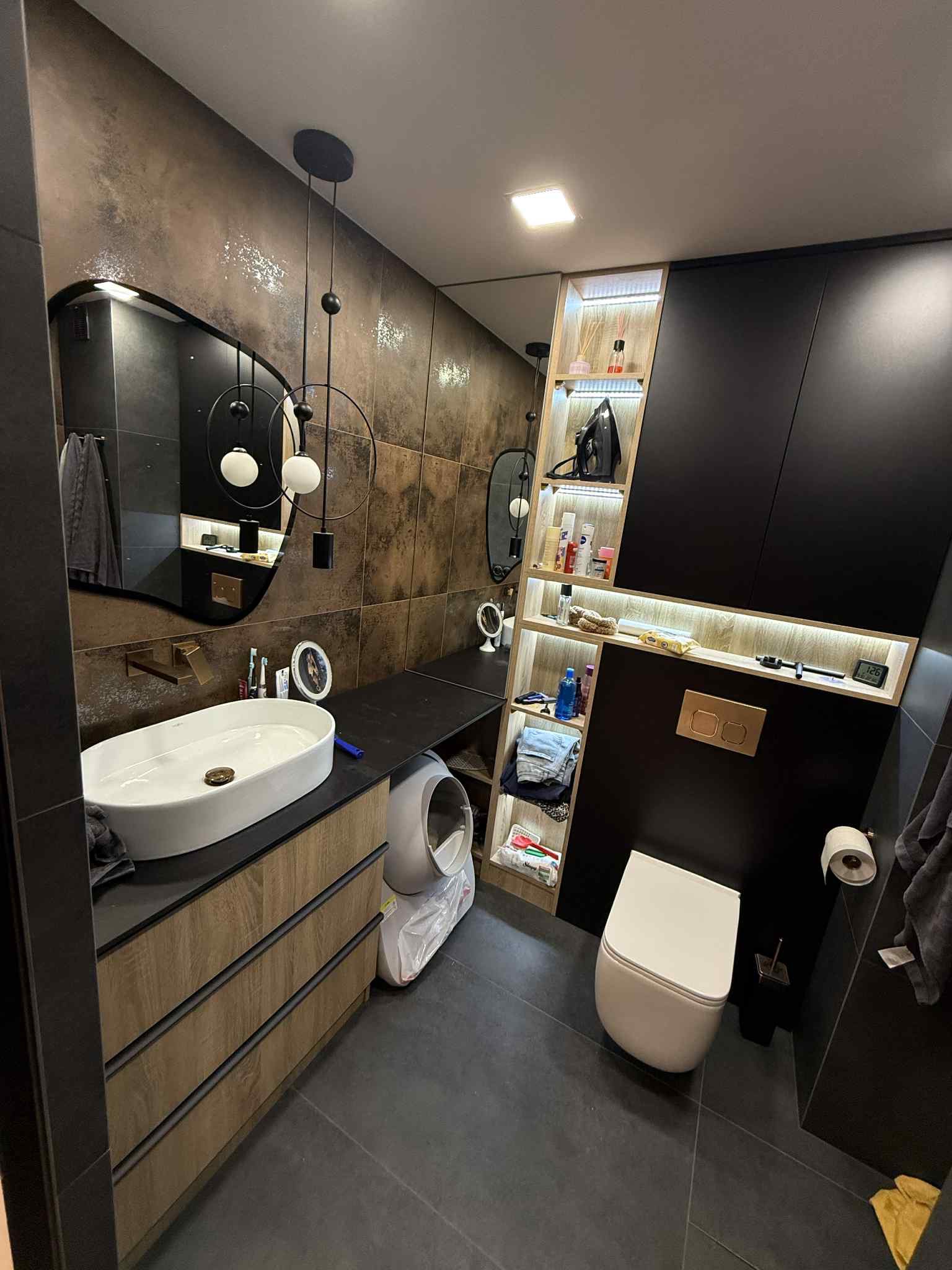 Nowoczesna łazienka z umywalką nablatową, szafką z drewnianymi frontami i czarnymi akcentami. Lustro z oświetleniem i półki z podświetleniem LED.