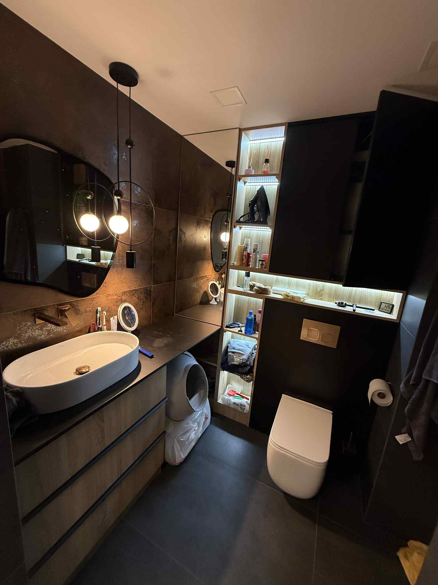 Nowoczesna łazienka z umywalką nablatową, szafką z drewnianymi frontami i oświetleniem punktowym. Ciemne płytki i minimalistyczny design tworzą elegancką przestrzeń.