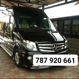 Cokolwiek - Czarny, lśniący Mercedes-Benz Sprinter, zaparkowany na zewnątrz, z widocznym numerem telefonu nałożonym na zdjęcie. Widoczny fragment budynku w tle.